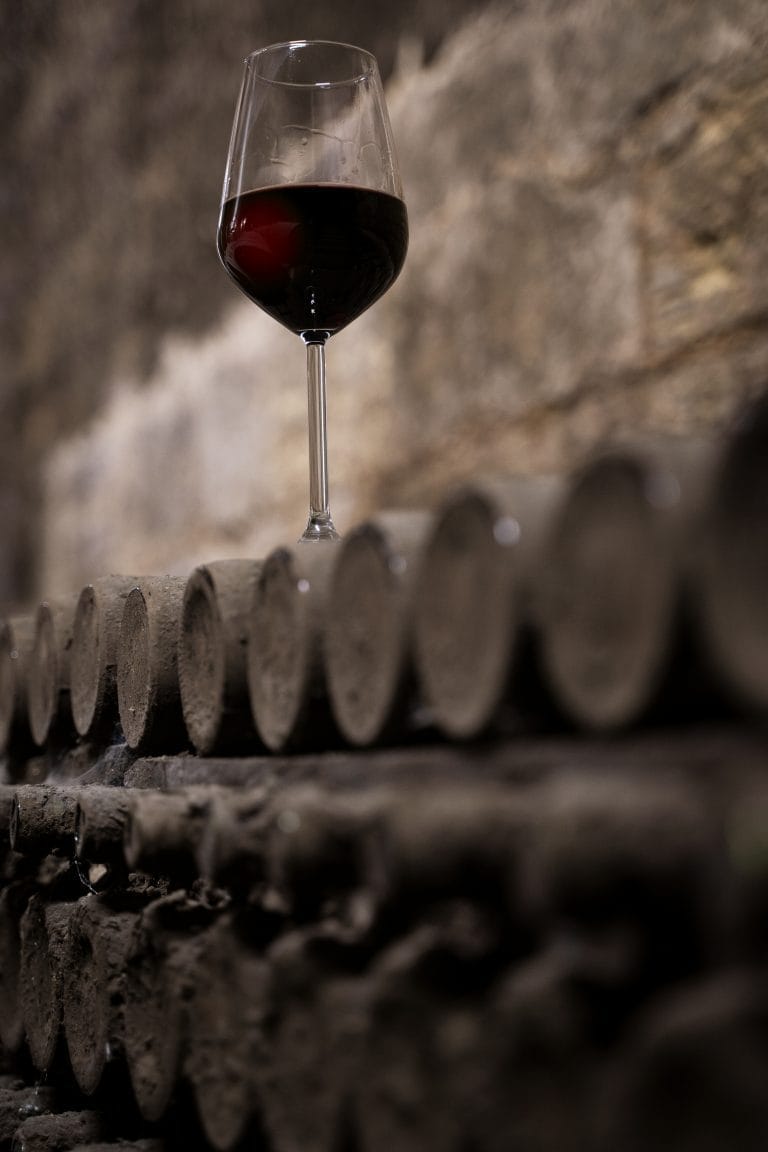 glass-with-red-wine-on-aged-wine-bottles-in-vintage-wine-cellar